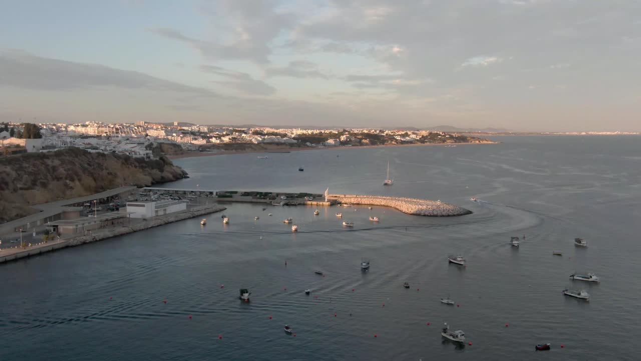 Aerial View of Boat leaving Harbor during Sunset. View Over Ocean with Beach and Town in the distance