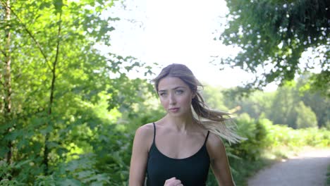 una mujer rubia, joven y en forma se concentra con los ojos enfocados hacia adelante mientras trota en un parque