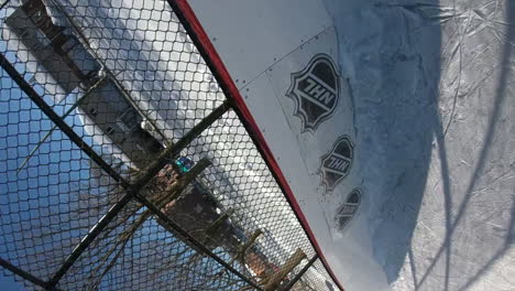 unique view of a puck firing into a hockey net during an outdoor game on an ice pad