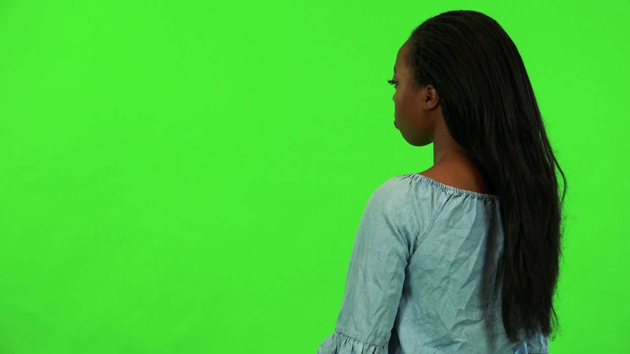 Uma jovem mulher negra de costas para a câmera olha ao redor - estúdio com tela verde.