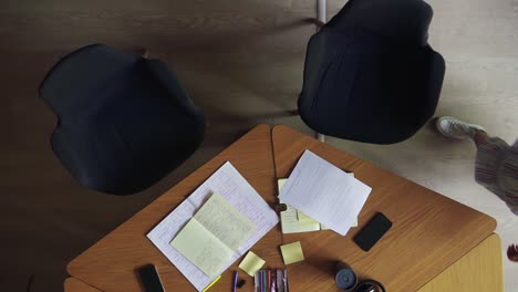 Two-unrecognizable-females-coming-and-sit-on-chairs,-starting-hands-writing-notes-in-notepad.-Writing-down-business-ideas.-Top-view-of-two-business-woman-hand-write-notes.-Women-in-white-blouses-sitting-at-the-wooden-table