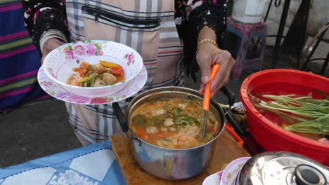 thai woman ladling tom yum soup into bowl to be served as healthy meal