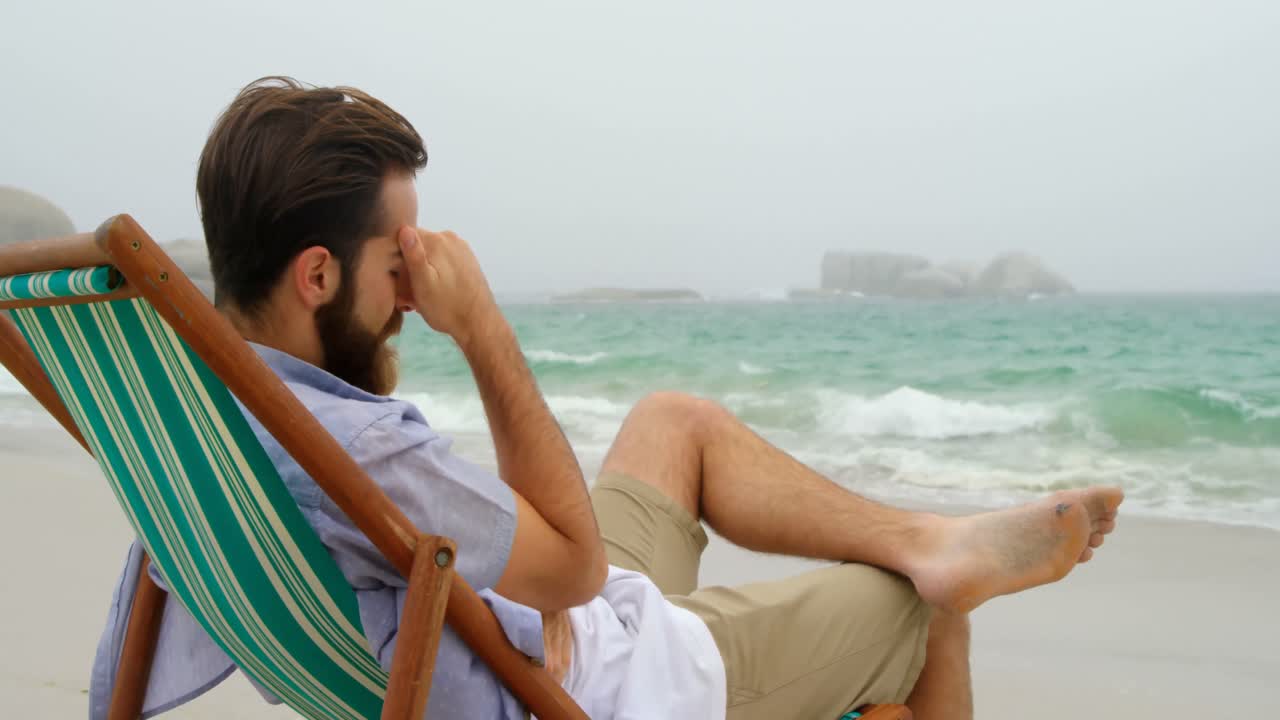 vista lateral de un hombre caucásico relajándose en una tumbona en la playa 4k