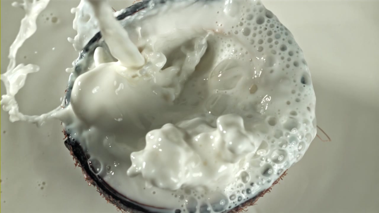 Versamento al rallentatore di latte di cocco in una metà di cocco fresco
