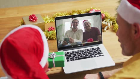 Padre-Caucásico-Con-Hijo-Usando-Una-Computadora-Portátil-Para-Una-Videollamada-Navideña,-Con-La-Familia-En-La-Pantalla