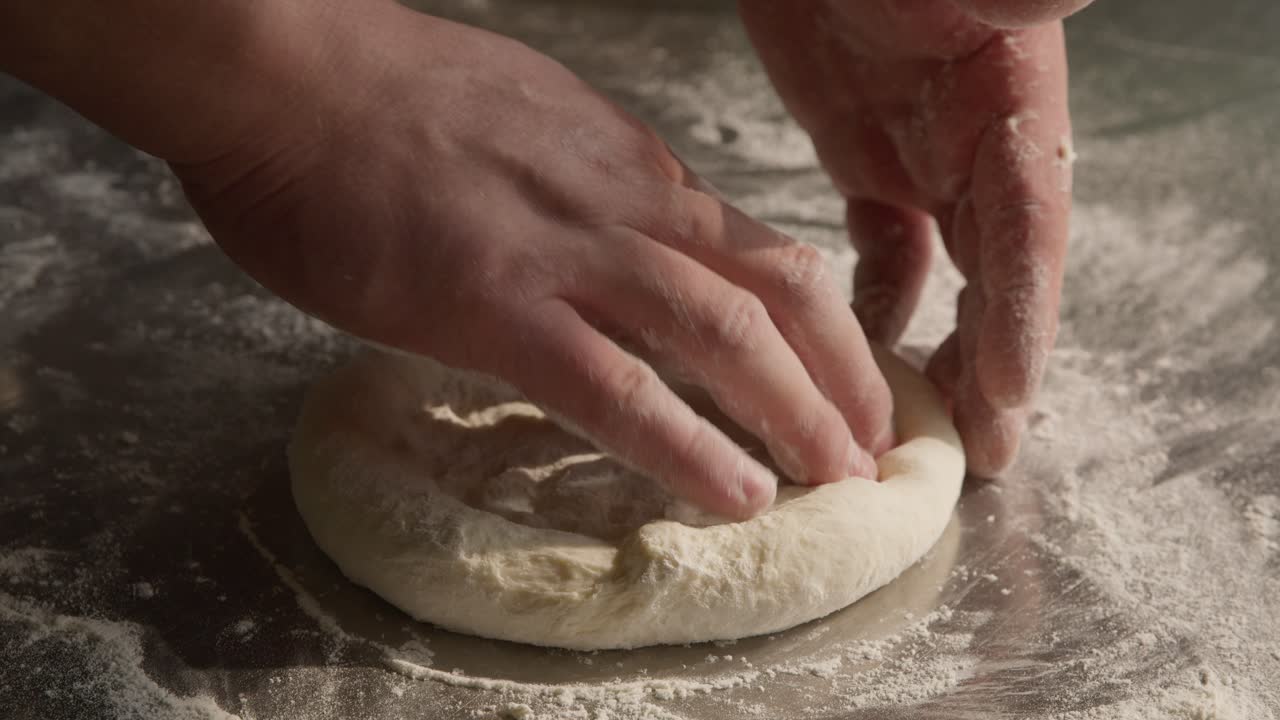 Male hands kneads the dough in closeup with flour on table