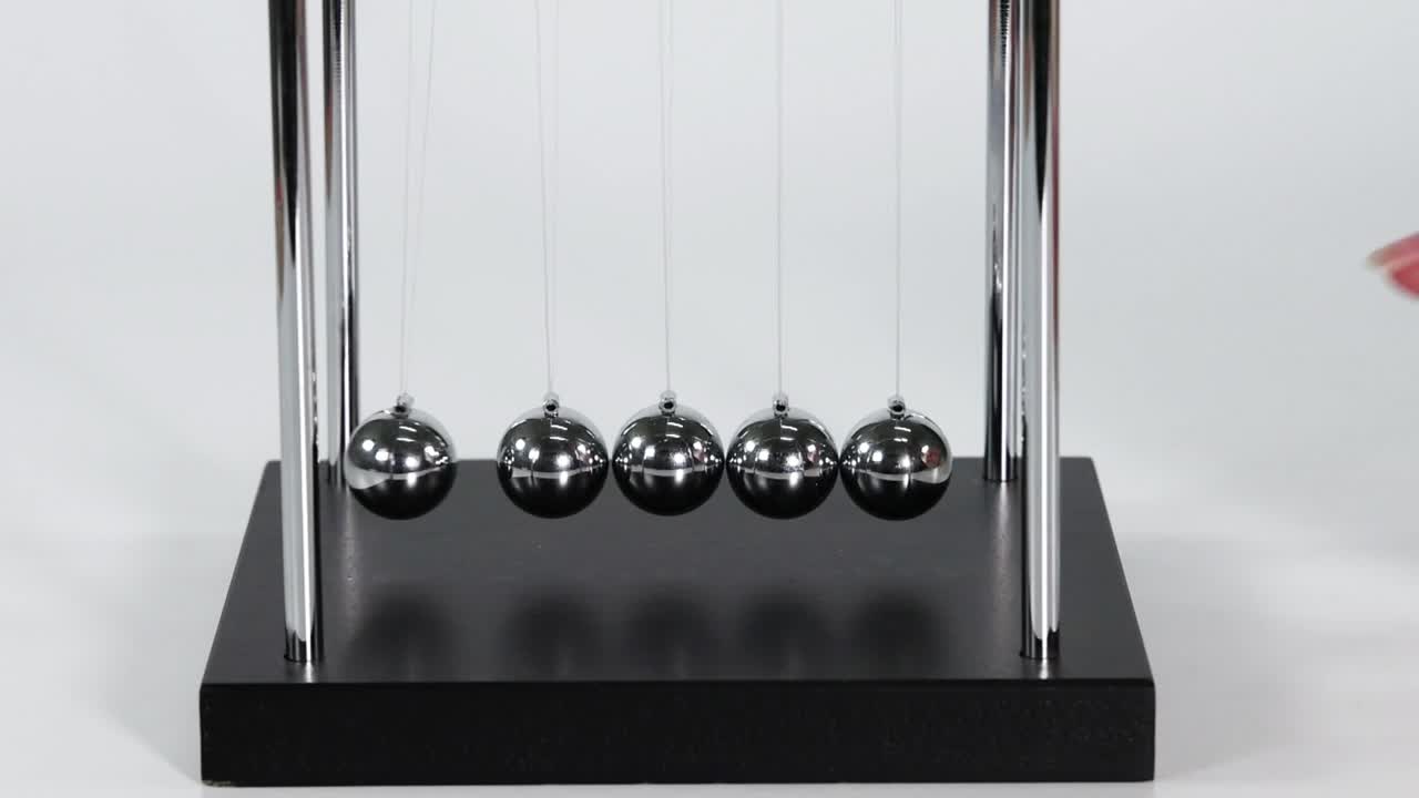 A hand pulls back a metal ball on a Newton's cradle to initiate movement