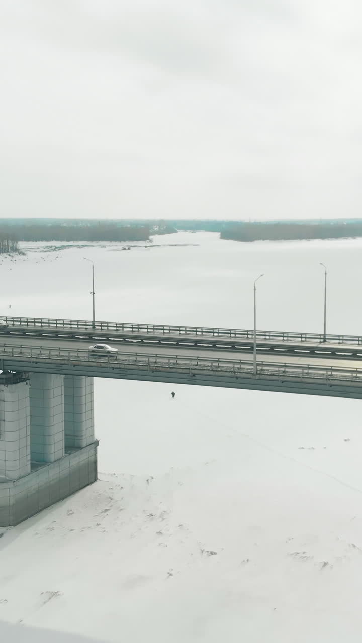 cars drive along large modern bridge over pictorial frozen river covered with white snow and ice aerial view