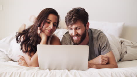 pareja relajándose en la cama con una computadora portátil