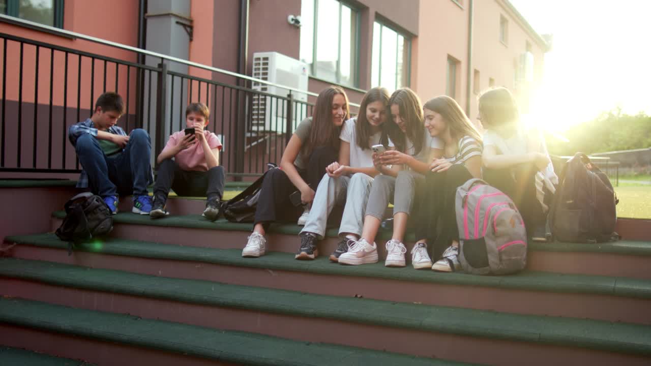Tenåringsstudenter koser seg og prater med mobiltelefonene sine i skolegården.