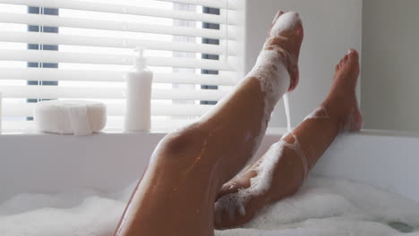 Low-section-of-african-american-woman-relaxing-in-the-bath-tub-in-the-bathroom-at-home