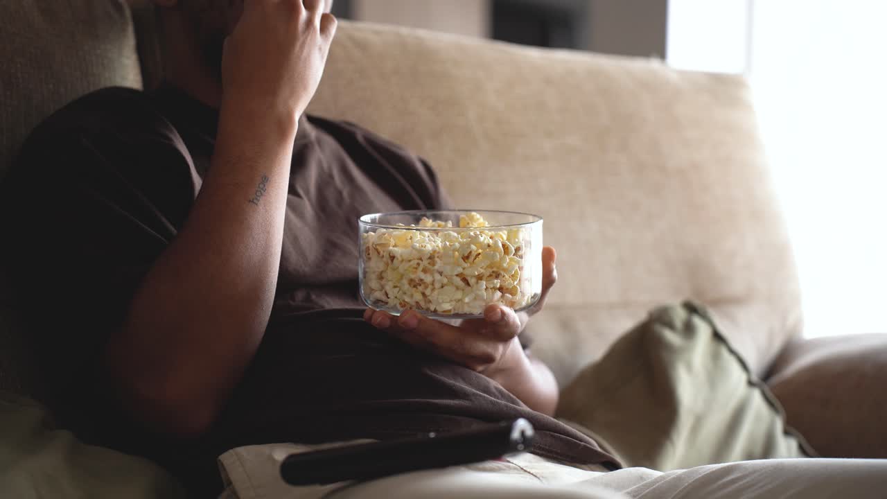 알 수 없는 남자가 포크콘을 먹고 소파에서 tv를 보고 있습니다.