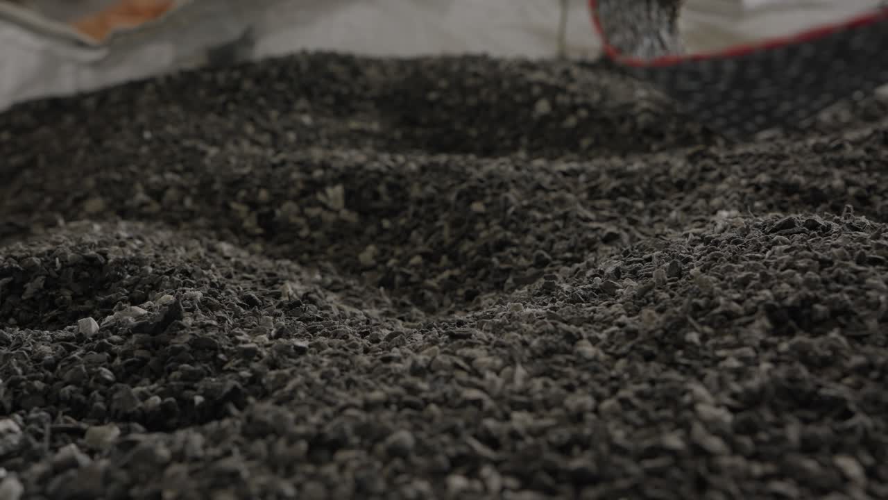 Pila densa di scaglie di plastica grigia finemente triturata raccolte all'interno di un saccone presso un impianto di riciclaggio.