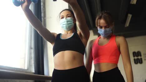 마스크를 착용 한 체육관에서 덤벨과 함께 일하는 여성