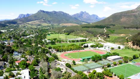 Rotierende-Luftdrohne,-Leichtathletikstadion-Der-Universität,-Leichtathletik,-Tennisplätze,-Berge,-Bäume-Und-Nachbarschaft-Im-Hintergrund,-Stellenbosch,-Coetzenburg