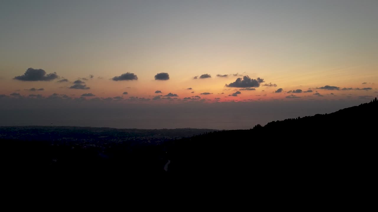 The sun sets over a stunning valley, casting warm hues in the sky. Soft clouds float above, creating a tranquil atmosphere. Nature's beauty unfolds as day turns to night