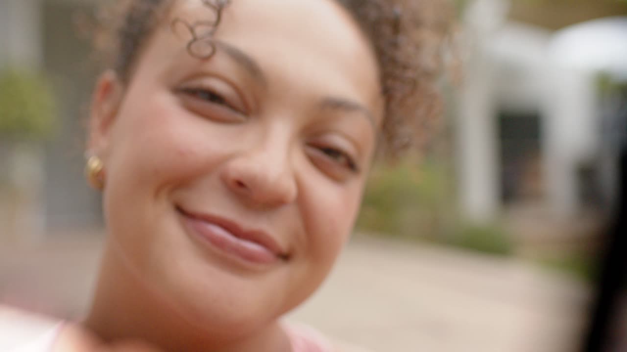 Mulher afro-americana reagindo à câmera se aproximando, rindo e esticando o dedo, com brincos de argola de ouro na varanda.
