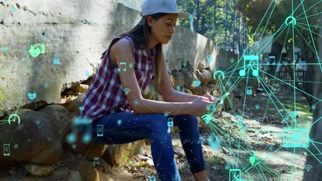 globe of digital icons spinning against woman using smartphone outdoors