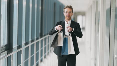 handsome man in business suit shows paper shopping bags