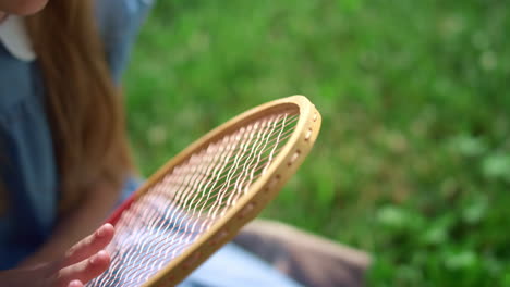 Closeup-girl-hand-touching-racket-strings.-Kid-sitting-on-lush-green-lawn