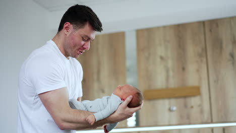 newborn sleeping in the big hands of his happy dad. smiling caucasian man waving his baby. low angle view.