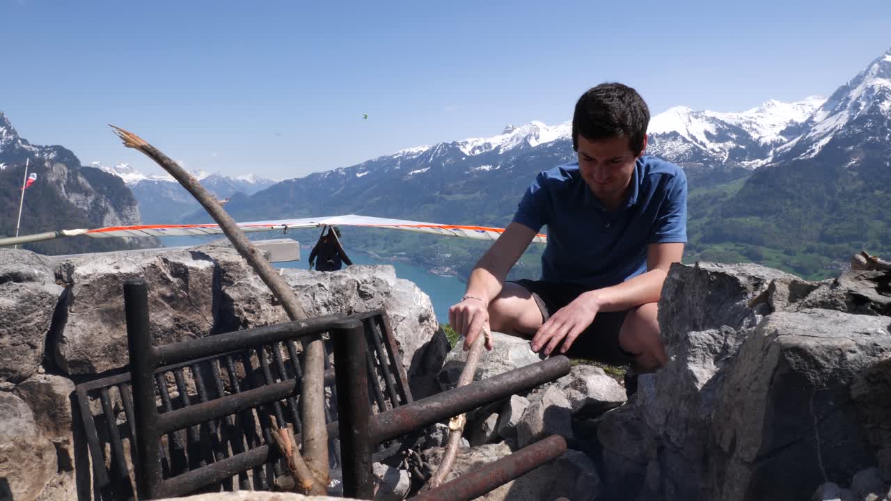 모닥불 위에 소시지를 굽고 있는 파란색 셔츠를 입은 청년의 중간 샷