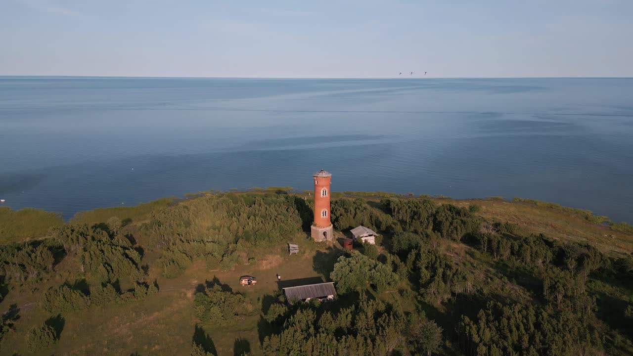 Fly away aerial drone flight from old lost place lighthouse at the coast of baltic sea - Estonia in Europe - nature helicopter flyover establishing shot summer 2022 - bird view