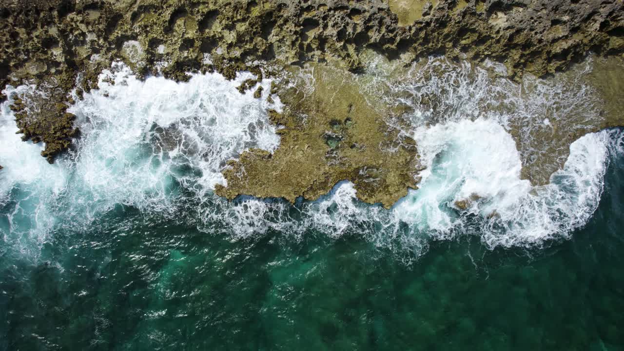 Aerial top-down trucking shot of the ocean waves crashing on the volcanic rocks