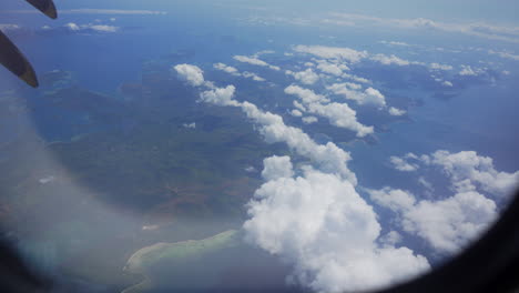 hand opens the airplane window revealing terrain, sea and clouds