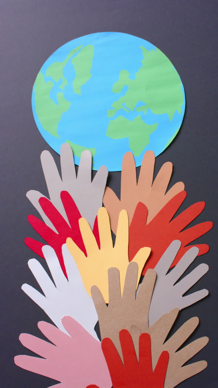 Vertical video of hands with globe made of colourful paper on gray background with copy space
