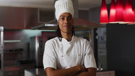 cocinero de raza mixta de pie en la cocina mirando a la cámara y sonriendo