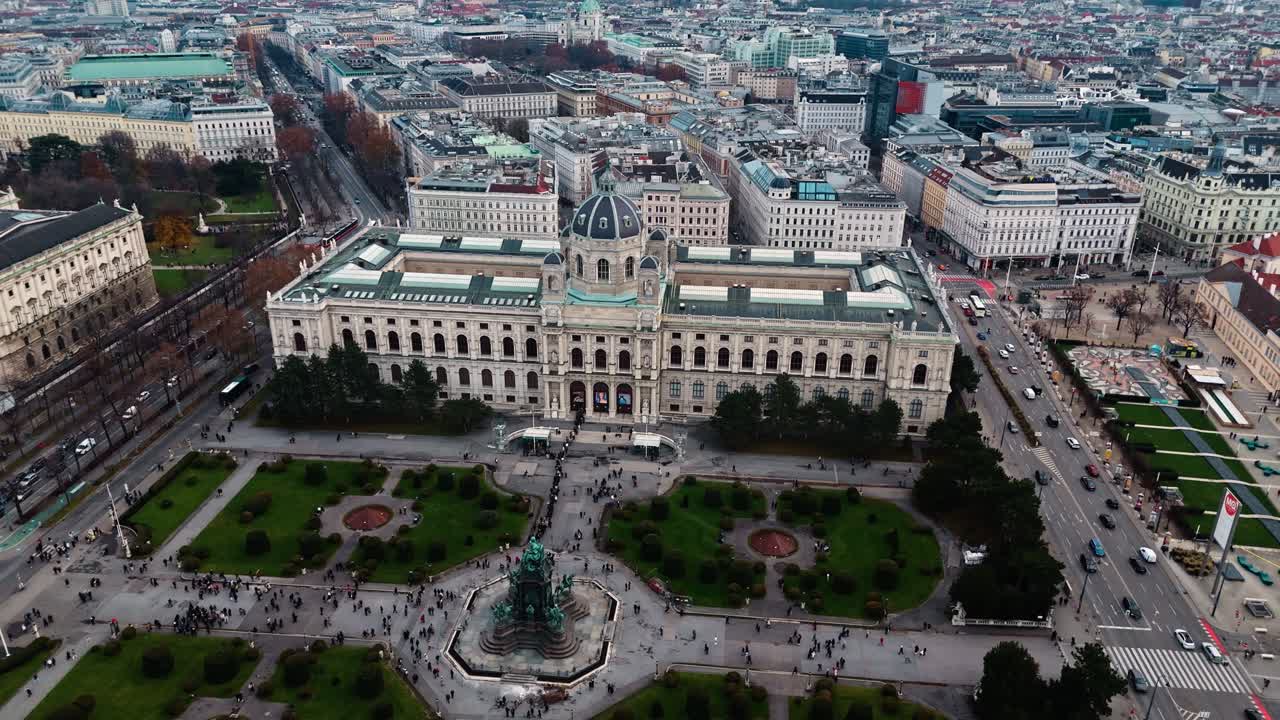 Ripresa aerea con drone con panoramica a destra sul Museo di Storia Naturale austriaco a Vienna, che mostra la sua imponente facciata e le strade circostanti, con il paesaggio urbano di Vienna visibile sotto la luce solare invernale.