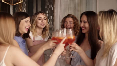 six beautiful stylish women in elegant casual outfit celebrating and drinking alcohol cocktails. cheers. beautiful, modern interior. hen party. slow motion