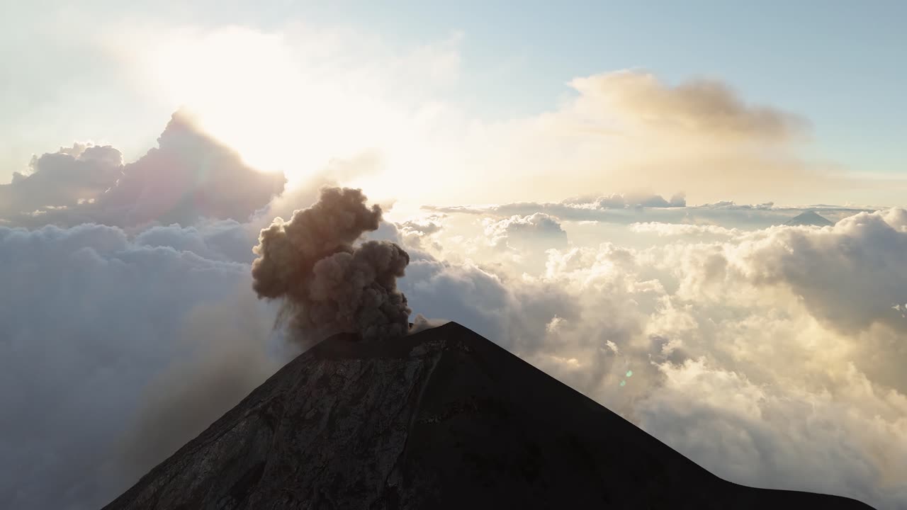 Majestic Fuego volcano peak with smoke rise, aerial orbit view above clouds