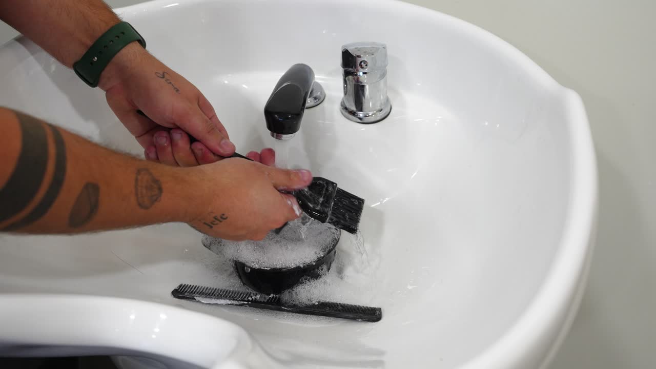 Close-up of hairdresser hands washing spatula, bowl and comb under sink water after bleaching application