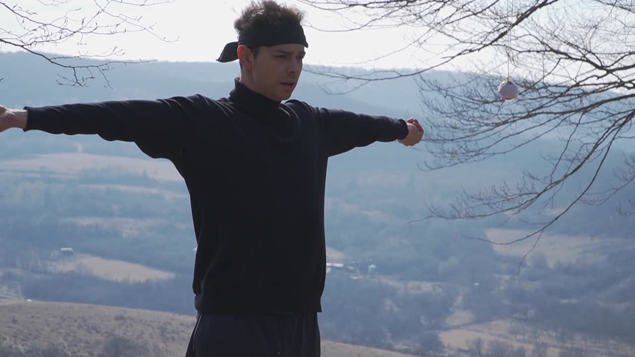 "A captivating outdoor shot of a person with arms extended, holding a tethered ball against rolling hills and trees. Ideal for sports, balance, and creative projects.