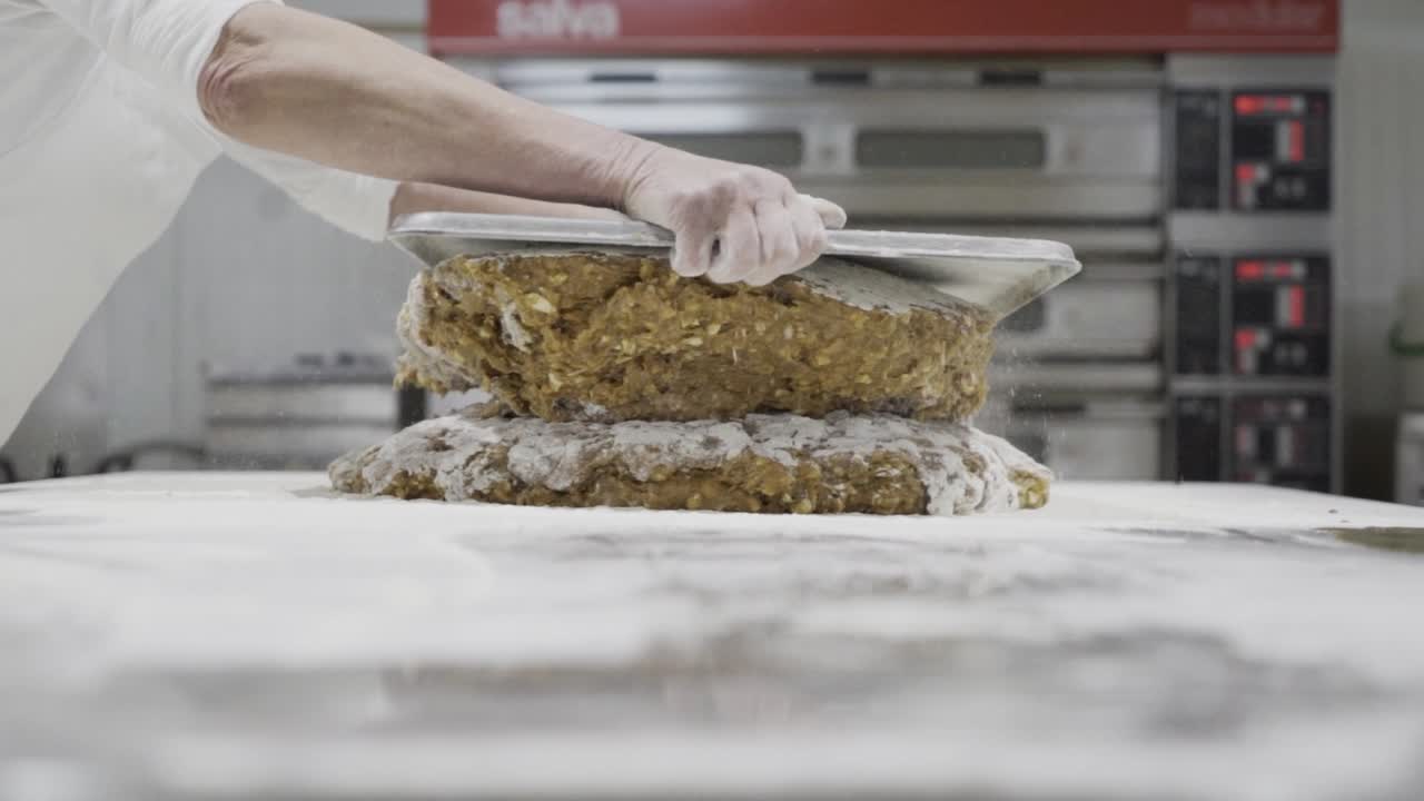 Slow motion panning shot of a dough for sweets being stacked and portioned with a tablet by a baker in a sweets factory in medina sidonia