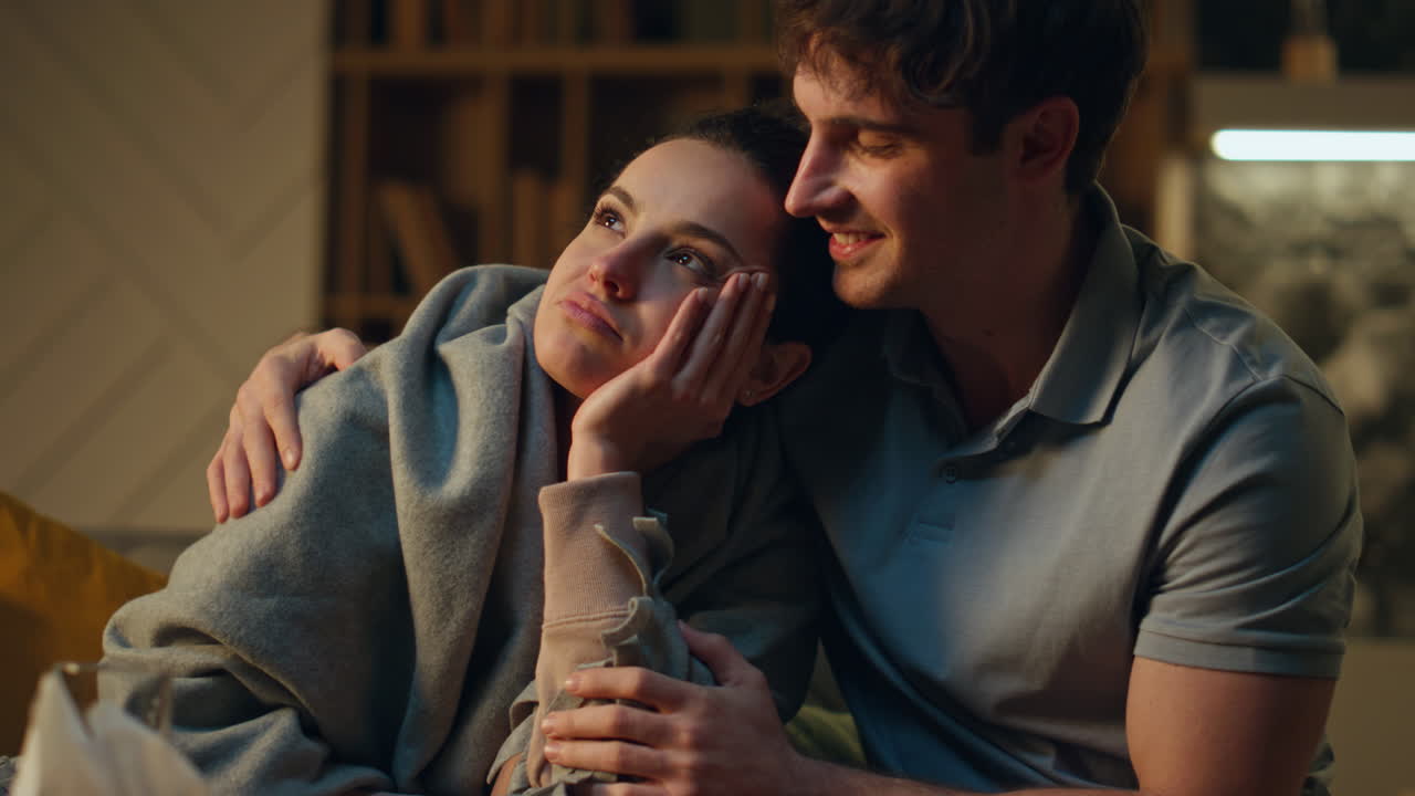 돌보는 남자가 건강하지 않은 여자친구를 포옹하고 집에서 소파에 앉아 있습니다.