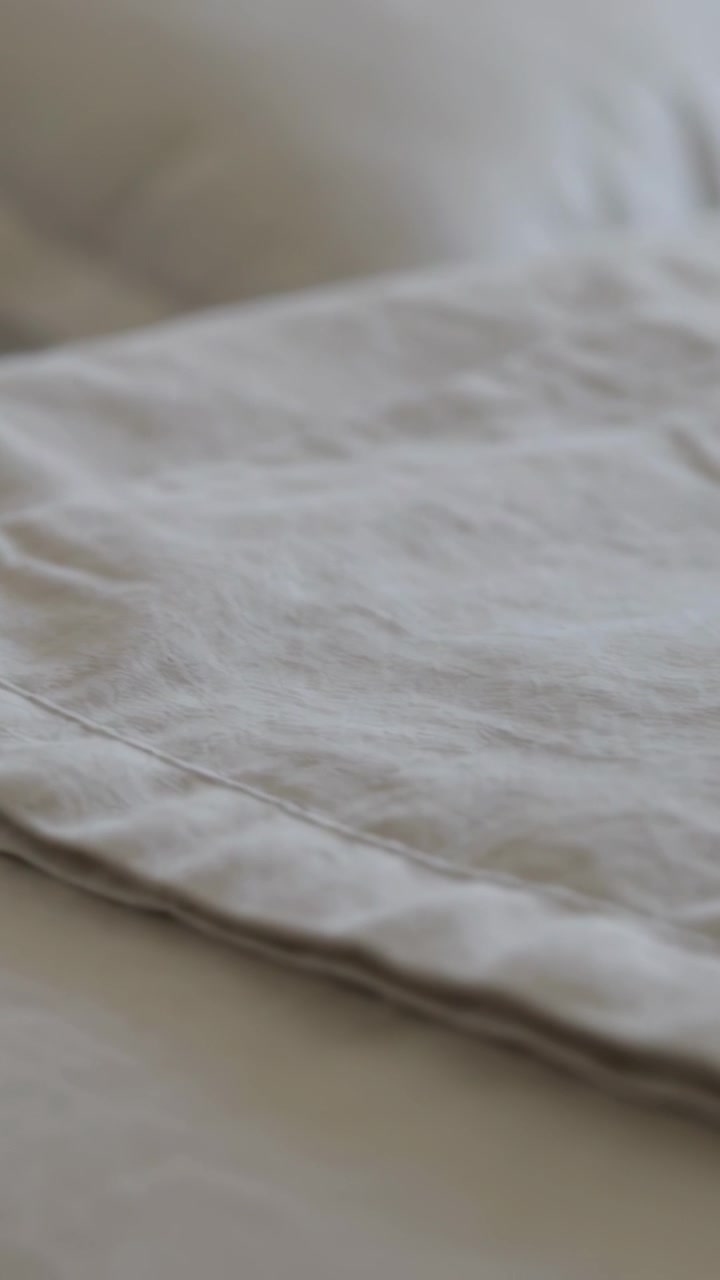 Vertical video: Panning camera showing linen sheet hem, pillow and bed in bedroom to show texture