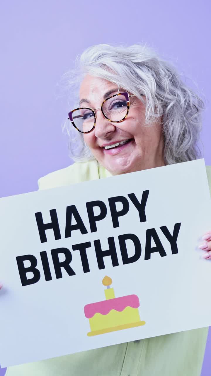 Donna anziana che tiene un cartello "Buon Compleanno" e sorride.