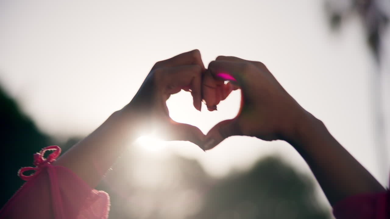 manos formando una forma de corazón contra el sol