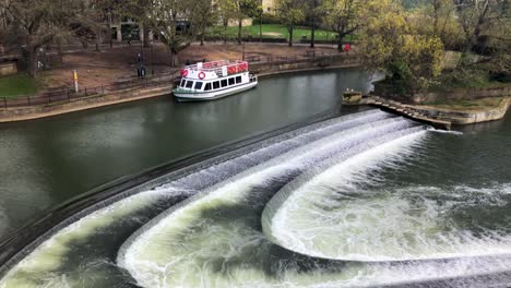 Vista-Panorámica-De-La-Presa-De-Pulteney-En-El-Río-Avon-En-Bath,-Somerset,-Reino-Unido-Con-Un-Barco-Turístico-Amarrado-A-Un-Lado---Tiro-Panorámico-Lento,-Aéreo