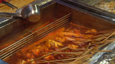 mano tomando oden picante coreano de la olla, comida callejera