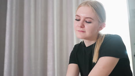 close up of young female massage therapist in black shirt with soft smile and concentrated expression, working in bright wellness room with curtain background during relaxing therapy session