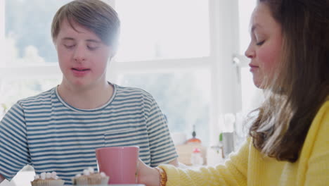 una pareja joven con síndrome de down disfrutando de té y pastel en la cocina de su casa.