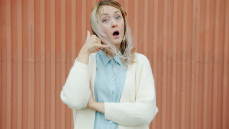 woman making a phone gesture in front of a wall