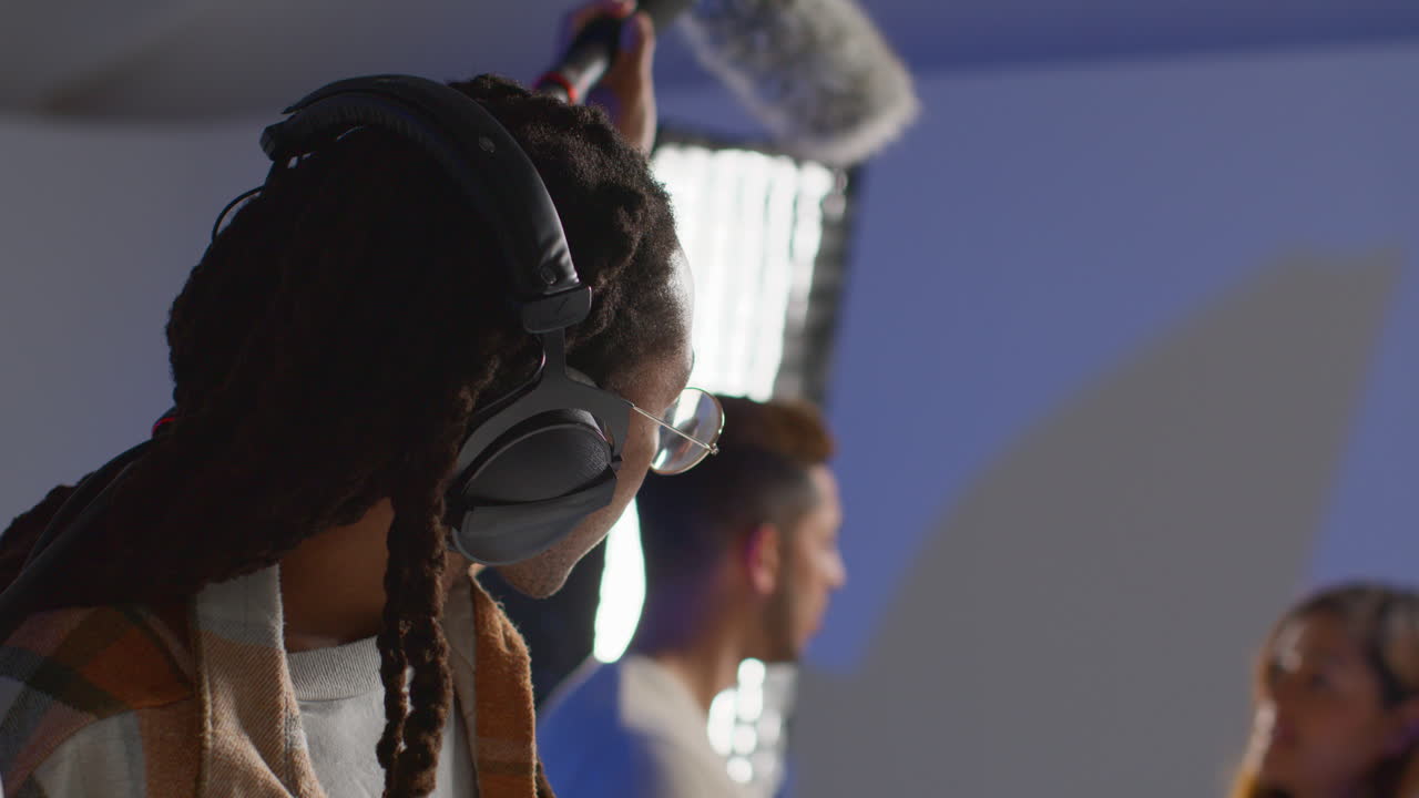 grabador de sonido de película masculino con auriculares sosteniendo un poste de micrófono por encima del actor filmando una película o video en el estudio