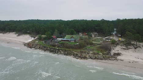 vista aérea de la costa del mar báltico en un día de invierno nublado, una casa en la playa con arena blanca, erosión costera, cambios climáticos, tiro de drones en órbita amplia