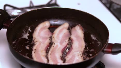 una cámara lenta de tres piezas de tocino cocinando en una sartén