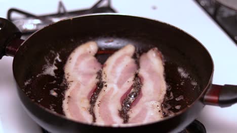 a slow motion of three pieces of bacon cooking in a frying pan